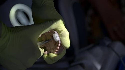 Slow motion vertical shot of a dentist wearing green latex gloves filing some veneers on a silicone