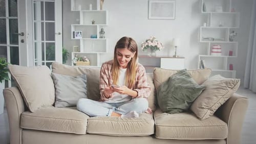 Smiling Woman Using Phone on Couch Indoors