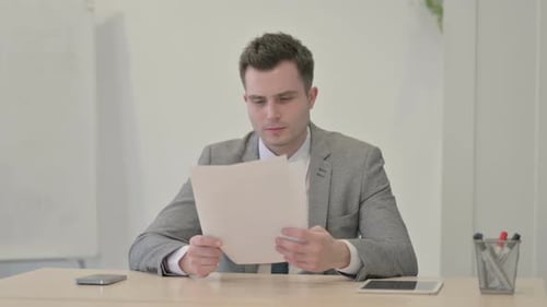 Young Businessman Reading Documents in Office, Paperwork