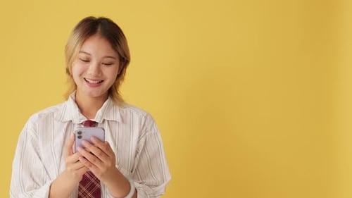 Smiling young woman using mobile phone isolated on yellow background in studio