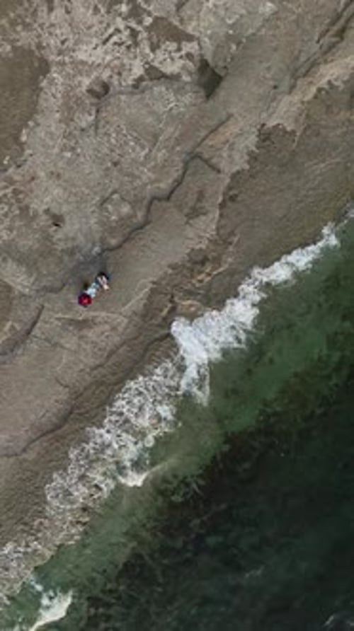 Vertical Video Coastal Retreat Aerial View of Couple Enjoying the Stony Beach Sunset