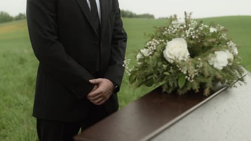 Man in Suit Stands Beside Coffin With Flowers