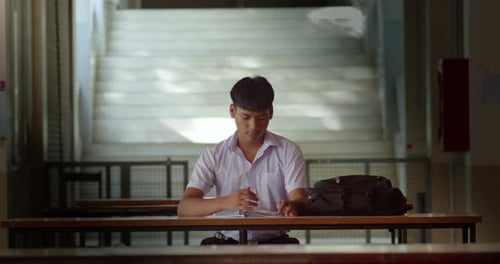A male high school student in a white school uniform is sitting and studying alone in preparation