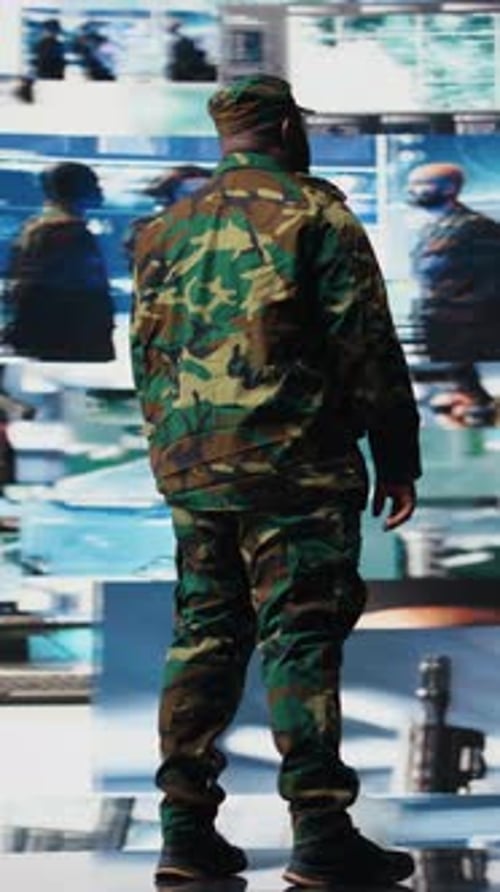 Man in Camouflage Uniform Standing Near Video Monitors