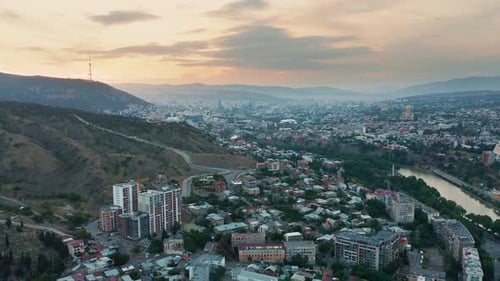 Aerial view of Tbilisi, Georgia and nearby mountains at sunset. Beautiful golden horizon. Pan to lef