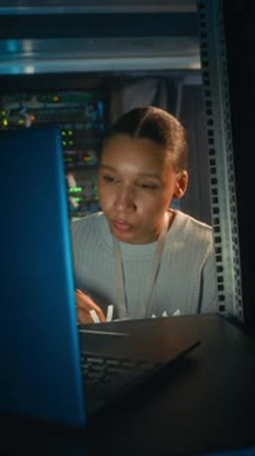 Technician Inspecting Cables Working on Laptop in Server Room