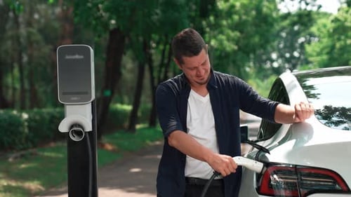 Man recharging battery for electric car during road trip. Exalt