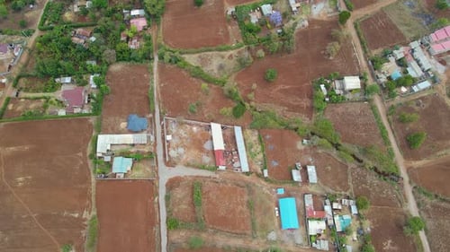 Aerial view of a town and sunlit fields, golden hour in rural Africa - tracking, drone shot. Green b