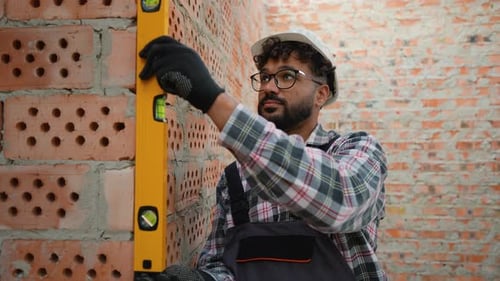 Builder Using Spirit Level on Brick Wall at Construction Site