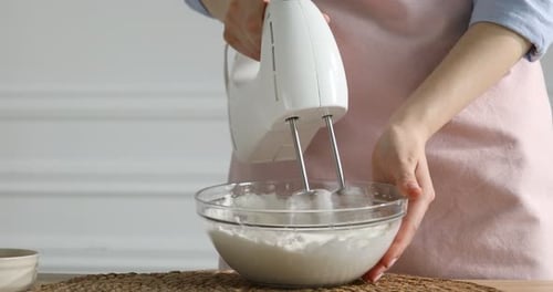 Woman whisking cream with hand mixer at table indoors, closeup. Space for text