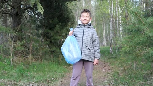 Niño sonriente con bolsa de basura de plástico después de talar el bosque para salvar el planeta