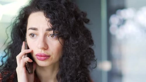 Close up of a serious curly brunette businesswoman talking on the phone in a office. A female