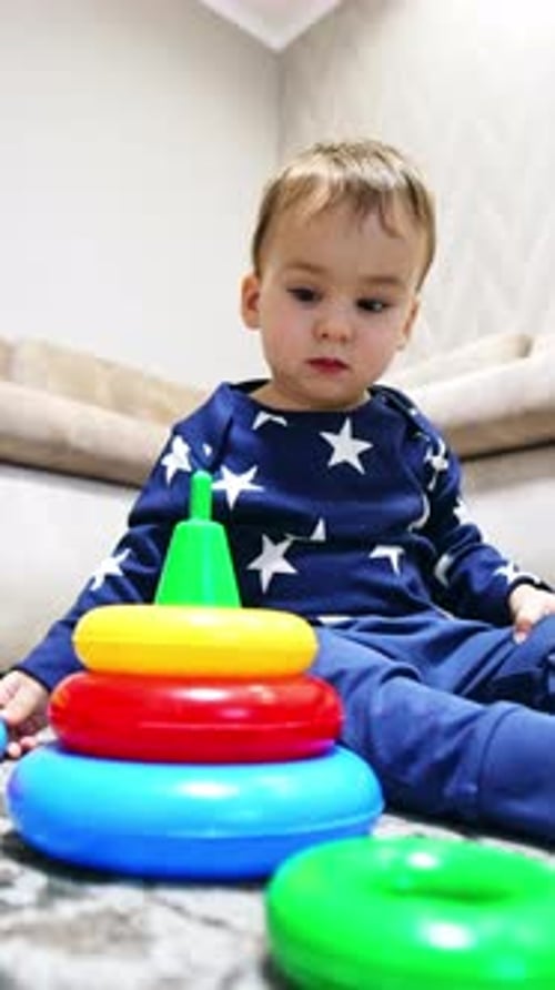 Спокойный симпатичный мальчик сидит на полу со своими игрушками.