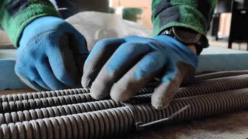 Foto aproximada de um homem com luvas montando cabos especiais no chão do canteiro de obras.