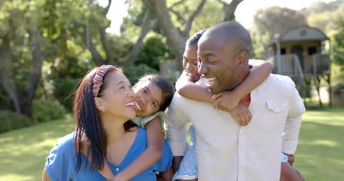 Smiling parents carrying children on backs, enjoying family time outdoors