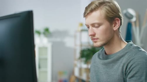 Porträt eines konzentrierten jungen Mannes, der von zu Hause aus an einem PC arbeitet.