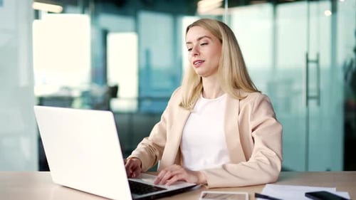 Happy young businesswoman finished work on laptop while sitting at workplace in modern office.