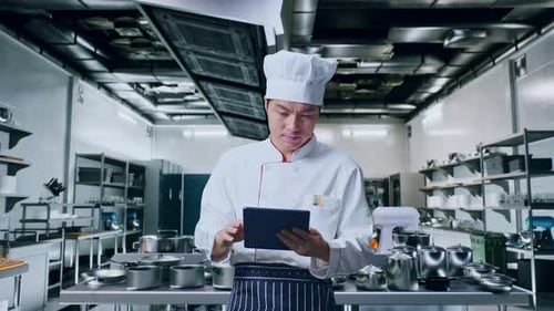 Asian Man Chef Using A Tablet In Kitchen