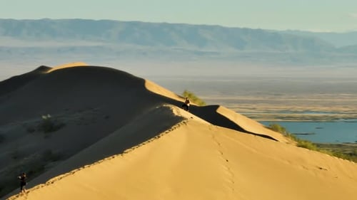 Person walking on a desert dune ridge with mountains in the background