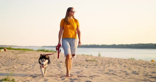 Young Woman Enjoying Evening Walk with Her Pet Dog on the Beach in Summer