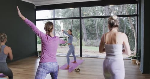 Focused diverse women stretching together on mats in yoga class with female coach, slow motion
