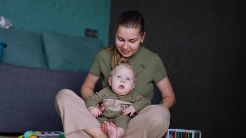 Frau sitzt mit ihrem Baby in den Händen auf dem Boden. Mutter klatscht ihrem Kind fröhlich in die Hände
.