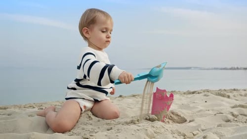 Little boy playing on the sandy beach with toys and using a shovel to dig sand