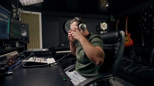 a focused male sound engineer wearing headphones sits at a mixing desk recording new track