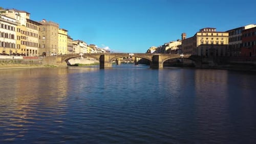 Aerial view flying low above Arno River under bridge on a sunny day in Florence in Italy in 4k.
