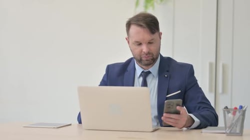 Man Uses Phone While Working at Desk