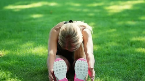 Fit woman doing stretching gym exercises on green grass in summer park morning