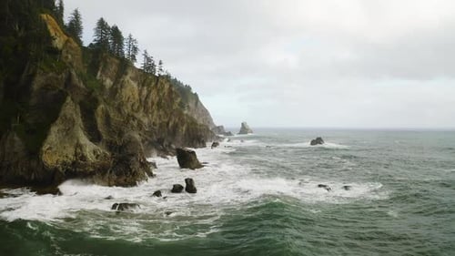 Pacific Ocean waves break against rugged, rocky Oregon coastline, static aerial.