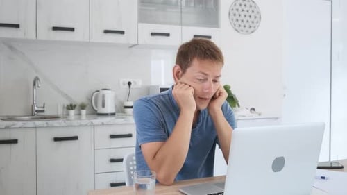 Stressed Man Working on Laptop in Modern Kitchen