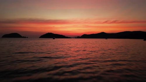 Flyover ocean with small islands in Thailand during sunset with dramatic orange sky
