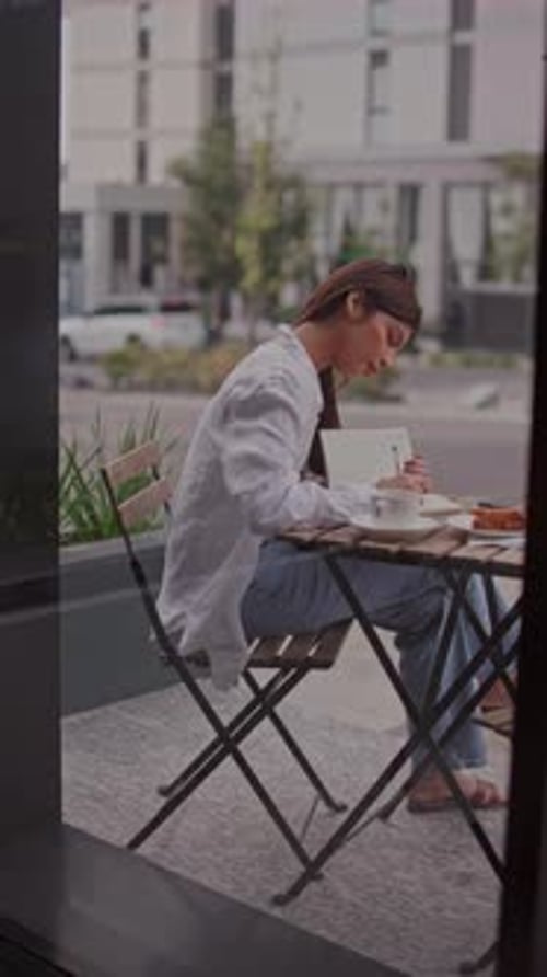 Young Woman Writing in a Notebook at an Outdoor Cafe Table