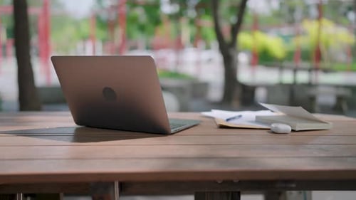 Close-up of laptop on wooden table outdoors with books, documents and pen on the documents.