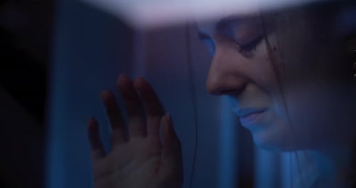 Sad Woman Leans Against a Glass Window at Night