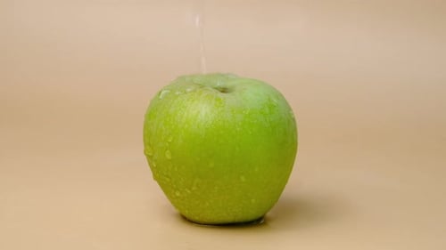Slow motion shot of water splashing on fresh green apple on beige background.