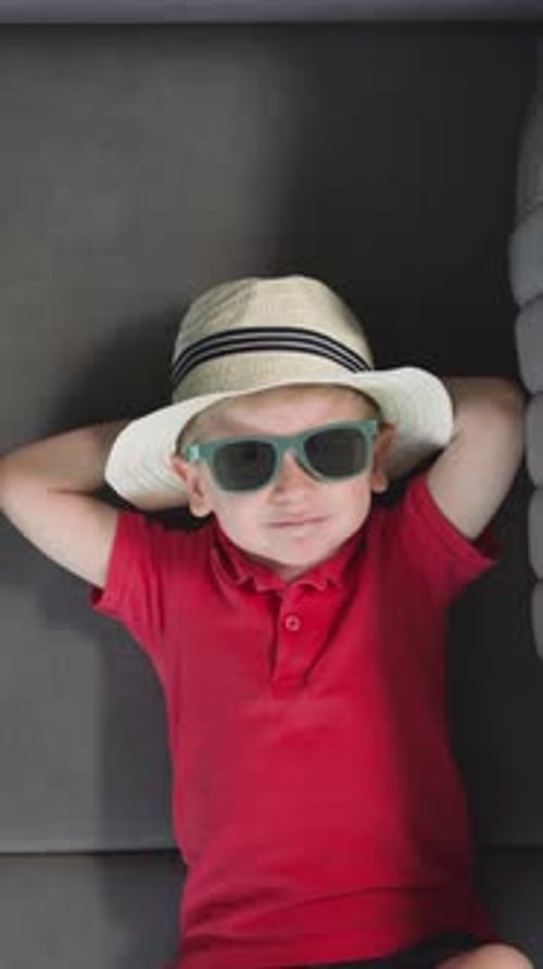 Child Lounging in Hat and Sunglasses on Couch
