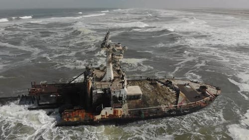 Rotación aérea alrededor de restos de naufragios y olas rompiendo.