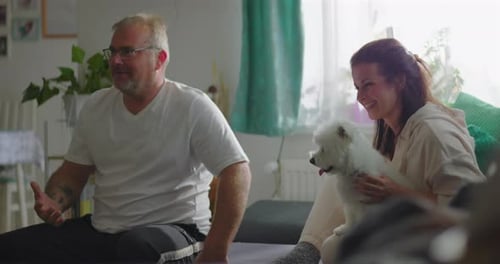 Smiling Couple Relaxing on Sofa with Small Dog