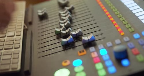 A hand operates a fader on a mixer in the recording studio