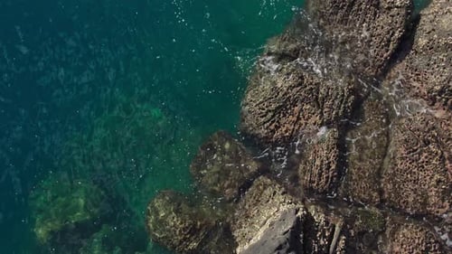 Top Down Drone Shot of Crystal Clear Ocean Water Splashing on Rocky Coast