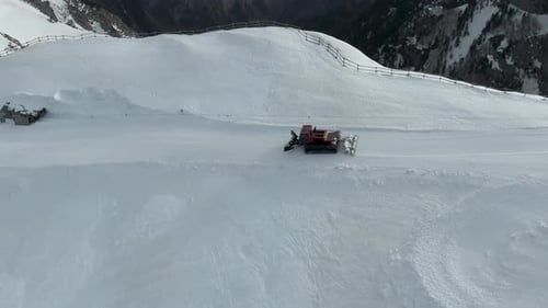 Pistenraupe fährt eine verschneite Straße entlang einer Bergklippe hinunter. Tolle Weitwinkelaufnahme aus der Luft von oben nach unten.