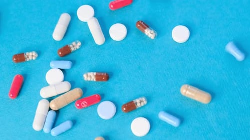 Colorful Pills and Capsules Falling onto Blue Surface