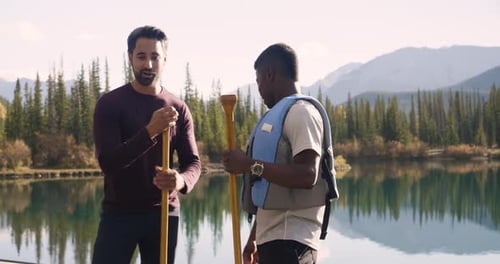 Male Friends With Paddle And Life Jacket Talking At Sunny Lake