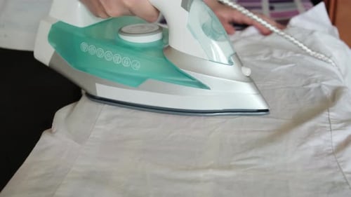 Female Hand Holding Electric Iron Ironing Clothes on Ironing Board