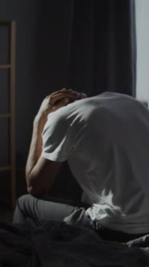 Adult in White Shirt on Bed Holding Head