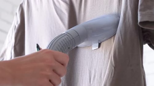 Nahaufnahme einer weiblichen Hand mit vertikalem Dampfgarer und T-Shirt