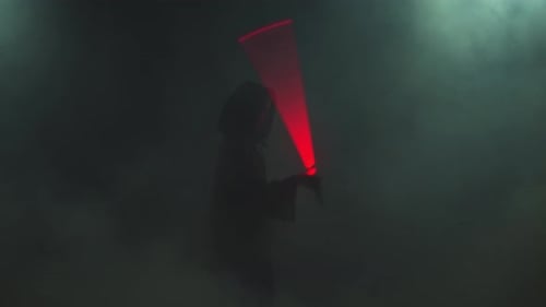 Young Man in Jedi Cosplay Costume with Lightsaber Battle on Black Background in Smoke and Rain Slow